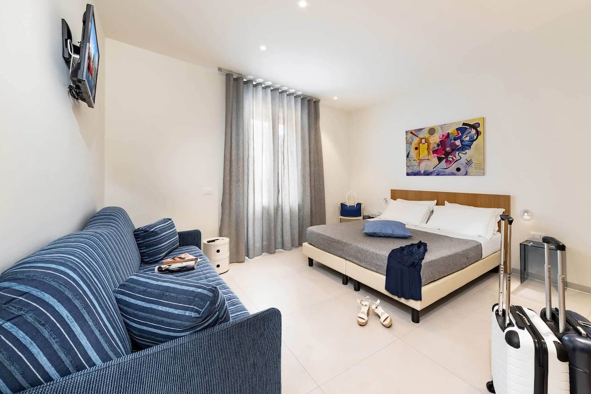 A modern hotel room with a bed, a sofa, a TV, and a painting on the wall.