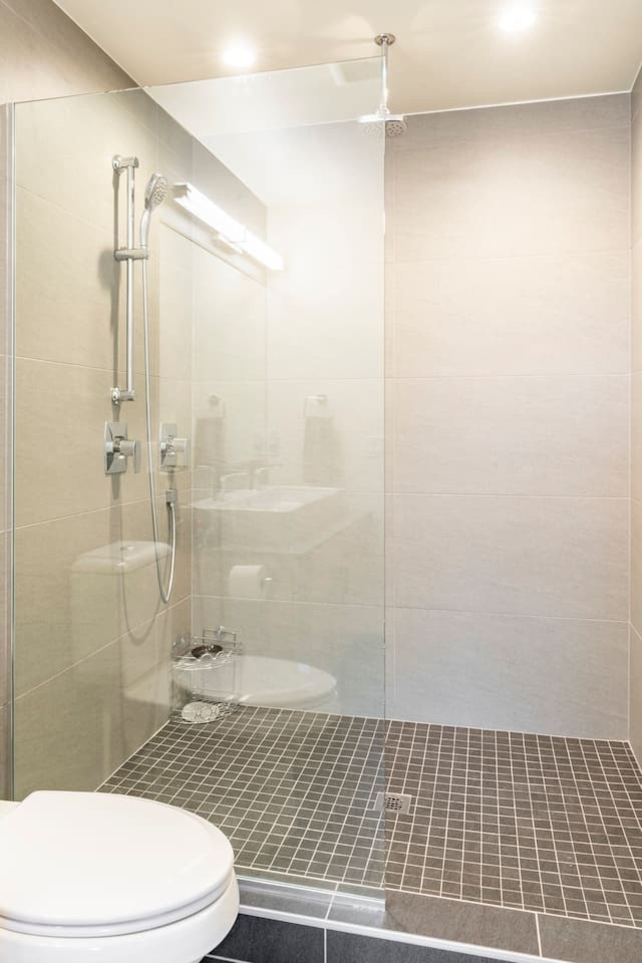 A modern bathroom with a glass-enclosed shower, a white toilet, and a tiled floor.