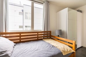 A bedroom with a wooden bed, a bedside lamp, a wardrobe, and a window with curtains. - The Imagination House! (Seattle)