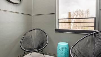 Ein Zimmer mit zwei schwarzen Gestellstühlen, einem türkisblauen Hocker und einem Fenster mit Blick auf Bäume.