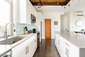 A modern kitchen with a central island, stainless steel appliances, and a wooden ceiling. - The Imagination House! (Seattle)