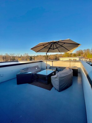 A rooftop patio with outdoor furniture, a large umbrella, and a view of the surrounding landscape. - The Imagination House! (Seattle)