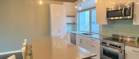 A modern kitchen with a central island, stainless steel appliances, and a wooden ceiling.