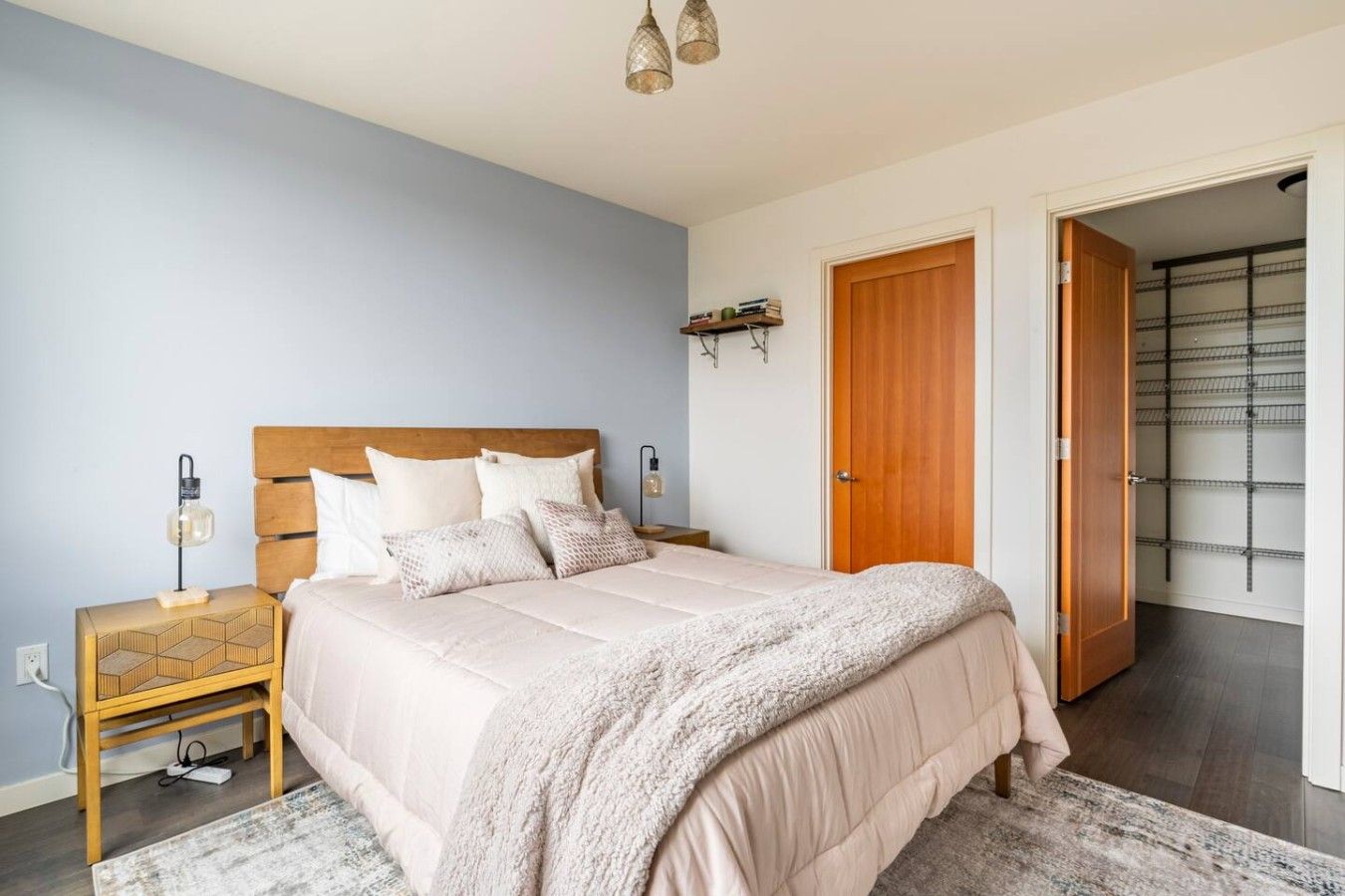 A bedroom with a bed, bedside tables, a nightstand, a lamp, a wall-mounted shelf, and a door leading to a closet.