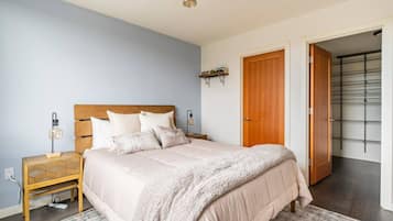 A bedroom with a bed, bedside tables, a nightstand, a lamp, a wall-mounted shelf, and a door leading to a closet.