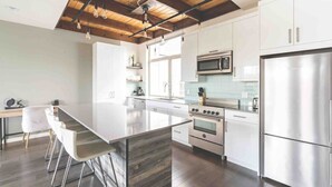 A modern kitchen with a central island, stainless steel appliances, and a wooden ceiling.