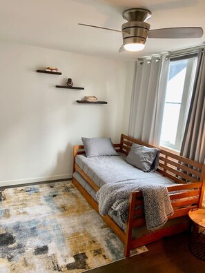 A small bedroom with a single bed, a ceiling fan, a window with curtains, and a rug on the floor. - The Imagination House! (Seattle)