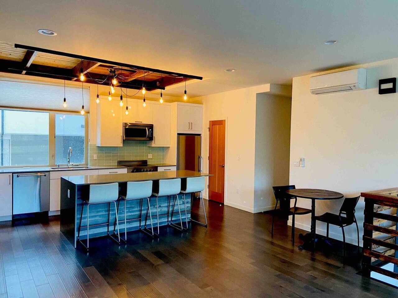 A modern kitchen with a bar area, wooden flooring, and pendant lighting.