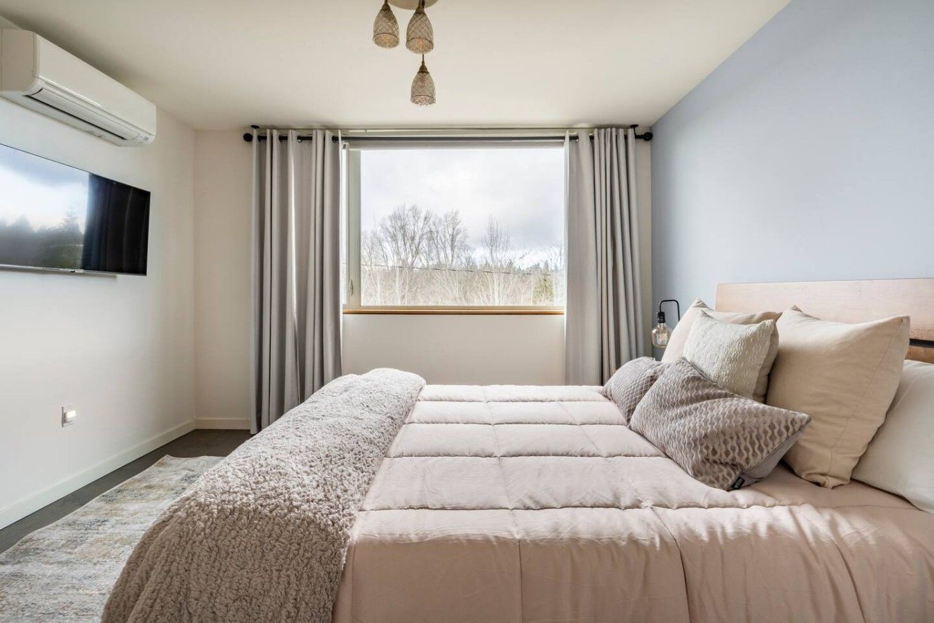 Ein Schlafzimmer mit einem großen Bett, einem an der Wand montierten Fernseher und einem Fenster mit Vorhängen.