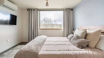 Ein Schlafzimmer mit einem großen Bett, einem an der Wand montierten Fernseher und einem Fenster mit Vorhängen.