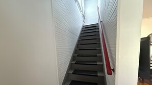 A narrow staircase with a red handrail, white walls, and a closed door at the top.