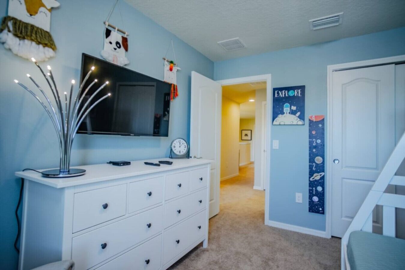 A child's bedroom with a dresser, a TV, a wall clock, and a space-themed poster.