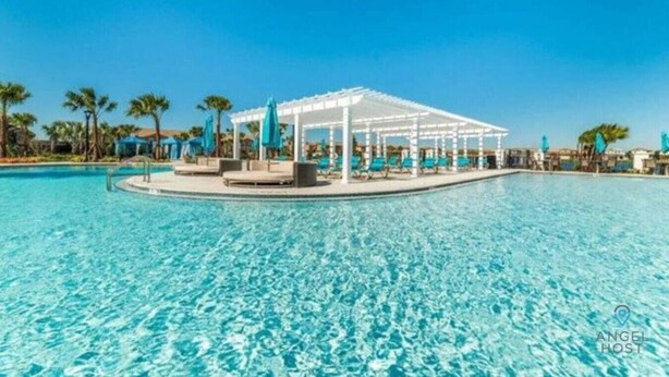 Una piscina amplia y luminosa con una pérgola blanca y sillones de descanso.
