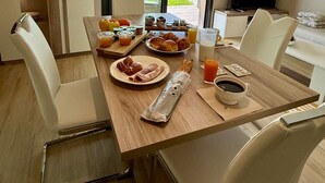 A dining area with a table set for breakfast, a television, and a view of a green landscape. - L'Annexe Coté Castagne du Domaine des Hauts de Rouquette (Eymet)