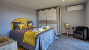 A modern bedroom with a large bed, a bedside table, a chair, and an air conditioning unit. - L'Annexe Coté Castagne du Domaine des Hauts de Rouquette (Eymet)