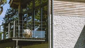 A two-story building with a stone facade, large windows, and a balcony with wicker furniture. - L'Annexe Coté Castagne du Domaine des Hauts de Rouquette (Eymet)