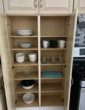A kitchen with wooden cabinets, shelves with plates, bowls, cups, and a blue cutting board. - 3BR Apartment, Split level house, in Waukegan, 7min. to The Naval Base with WiFi (Waukegan)