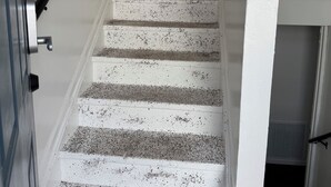 A staircase with white steps and black speckles, leading to a kitchen area with wooden cabinets and a window with curtains.