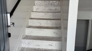 A staircase with white steps and black speckles, leading to a kitchen area with wooden cabinets and a window with curtains.