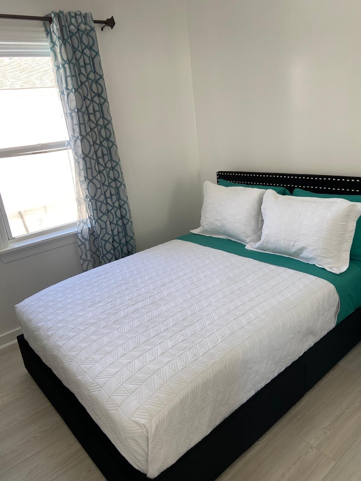 A bed with a white quilt, two white pillows, and a green bedspread.
