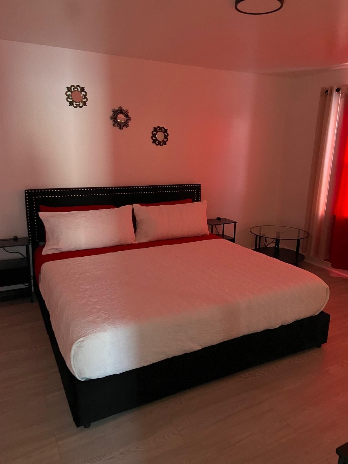 Una cama grande con cabecera negra y ropa de cama blanca, dos apliques de pared y una mesita de noche con una silla.