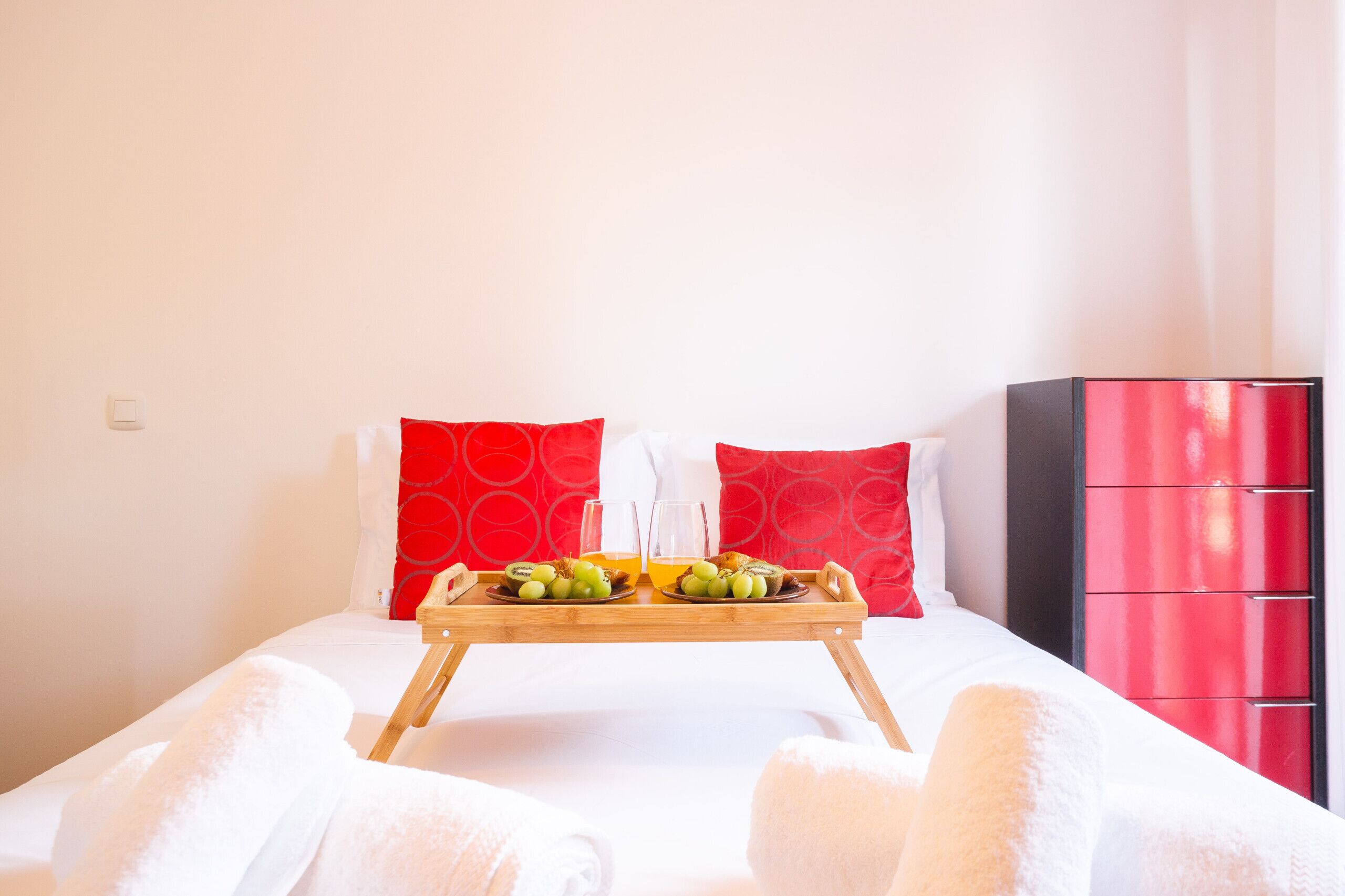 Una habitación de hotel con una cama, una bandeja con frutas y jugo, y un armario rojo.