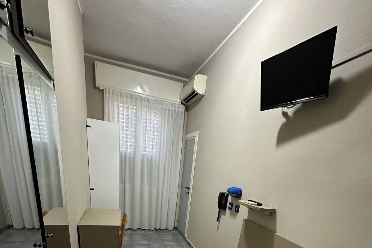 A room with a bed, a desk, a chair, a television, and an air conditioning unit.