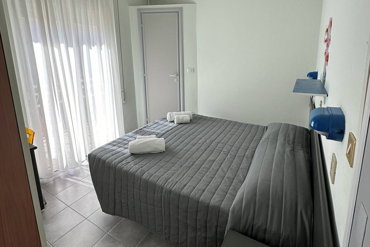 A hotel room with a bed, a bedside table, a wall-mounted air conditioner, and a door.