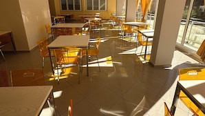Un vaste espace dédié à la salle à manger, avec de nombreuses tables et chaises, de grandes fenêtres laissant entrer la lumière naturelle et un design moderne au niveau du plafond.