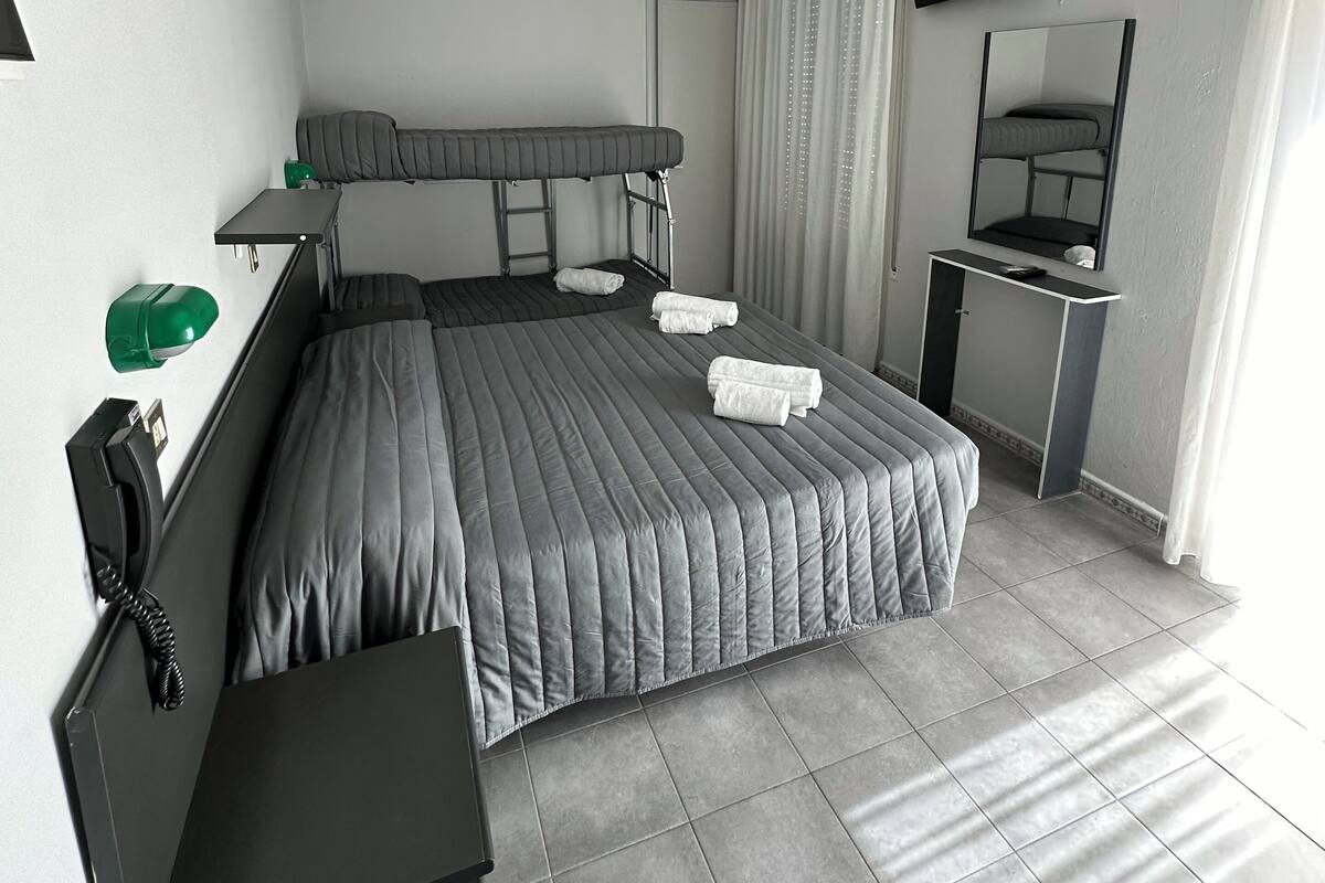 A modern hotel room with a large bed, a desk, a chair, a TV, and an air conditioning unit.