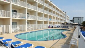 Ein Kreuzfahrtschiffdeck mit Schwimmbad, Liegestühlen und Balkonen.