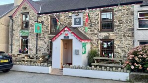A stone building with a small entrance, a sign for 'Tafarn Y Fic', and a flag.