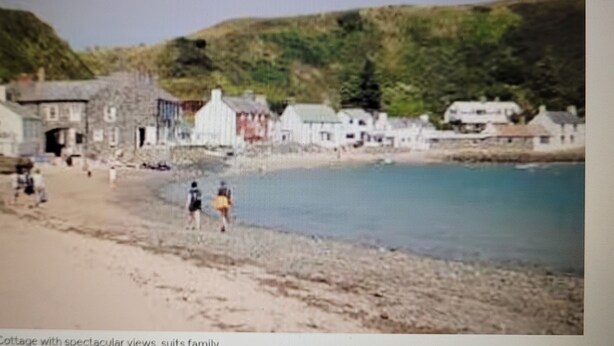 A coastal cottage with a beach view, stone buildings, and a rocky shoreline.