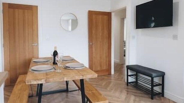 A dining area with a wooden table set for four, a bottle of wine, and a round mirror on the wall. - Cricketers View - West Yorkshire (Bradford)