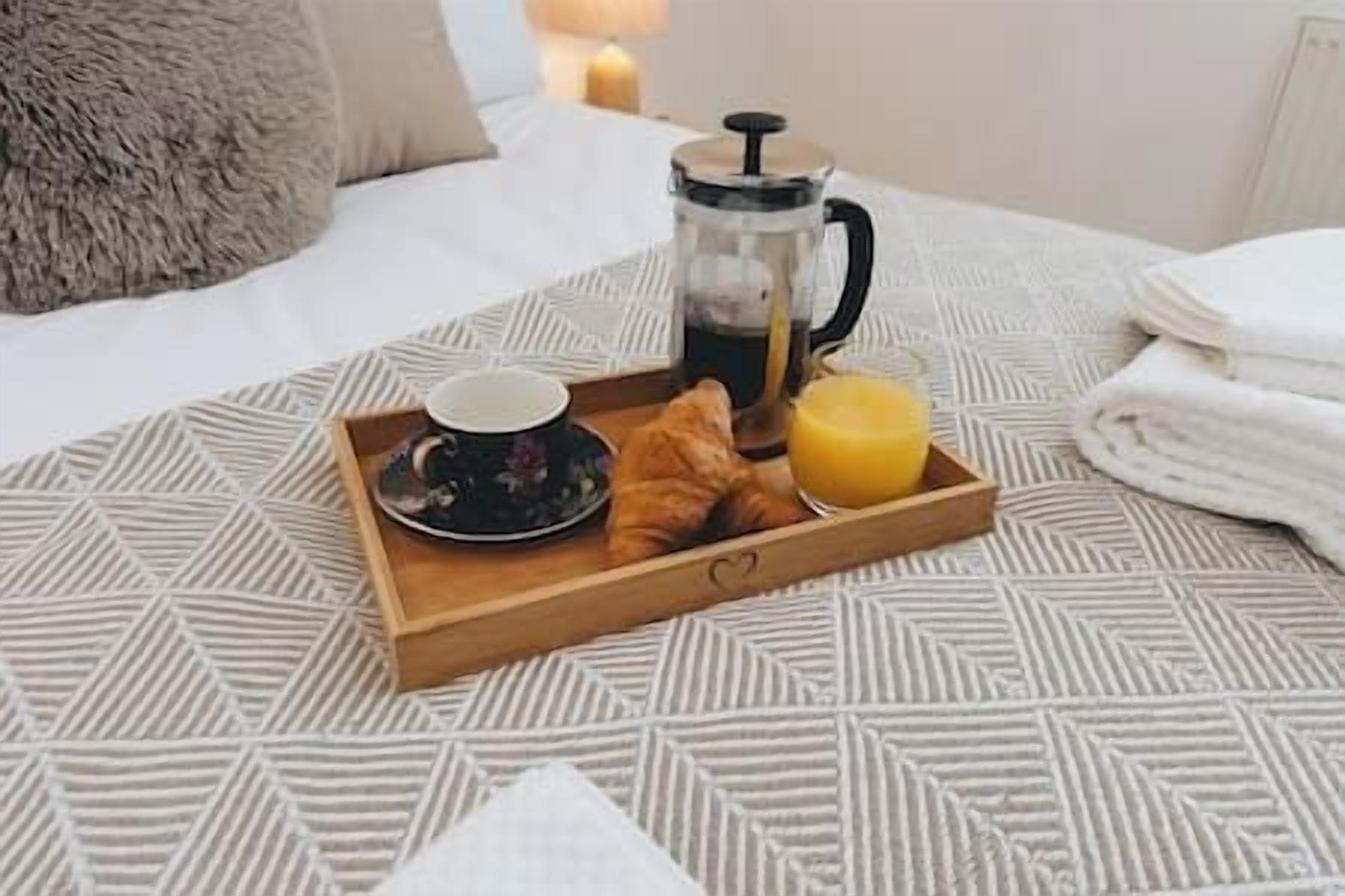 A breakfast tray with croissants, a cup, and orange juice on a patterned bedspread.