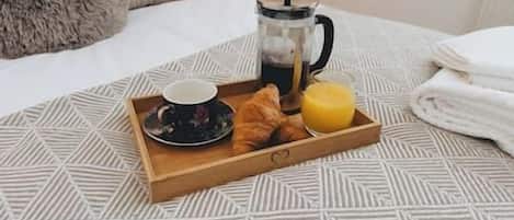 A breakfast tray with croissants, a cup, and orange juice on a patterned bedspread.