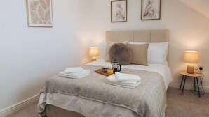 A bedroom with a bed, two bedside tables, a nightstand, and a wall-mounted lamp. - Cricketers View - West Yorkshire (Bradford)