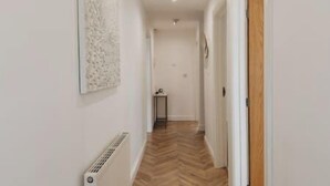 A narrow hallway with a herringbone floor, white walls, and a radiator. - Cricketers View - West Yorkshire (Bradford)