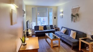 A modern living room with a wooden coffee table, two sofas with patterned cushions, a small side table, and a large window providing a view of the street. - Liverpool Street Apartments (London)