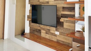 A modern living room with a large flat-screen TV mounted on a wooden wall, wooden beams on the ceiling, and a wooden floor.