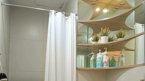 A bathroom with a shower, toilet, and a shelf with toiletries.