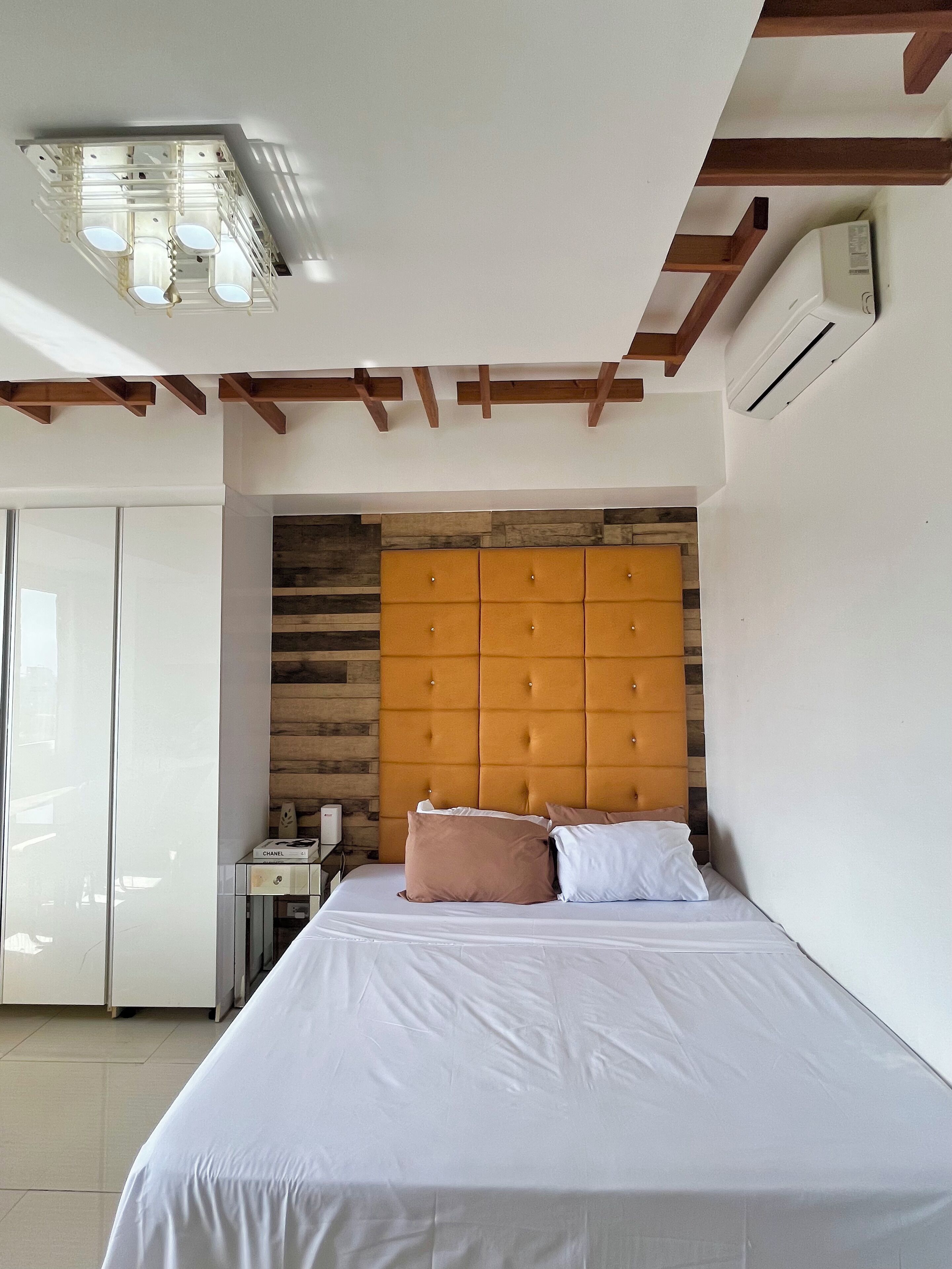 A bedroom with a bed, a wooden headboard, a wardrobe, and a ceiling light fixture.