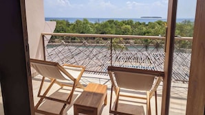 Een balkon met twee houten stoelen en een tafeltje, met uitzicht op een zwembad en weelderige begroeiing.