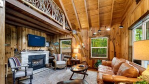Un interior de cabaña acogedor con chimenea, muebles de cuero y un televisor montado en la pared.