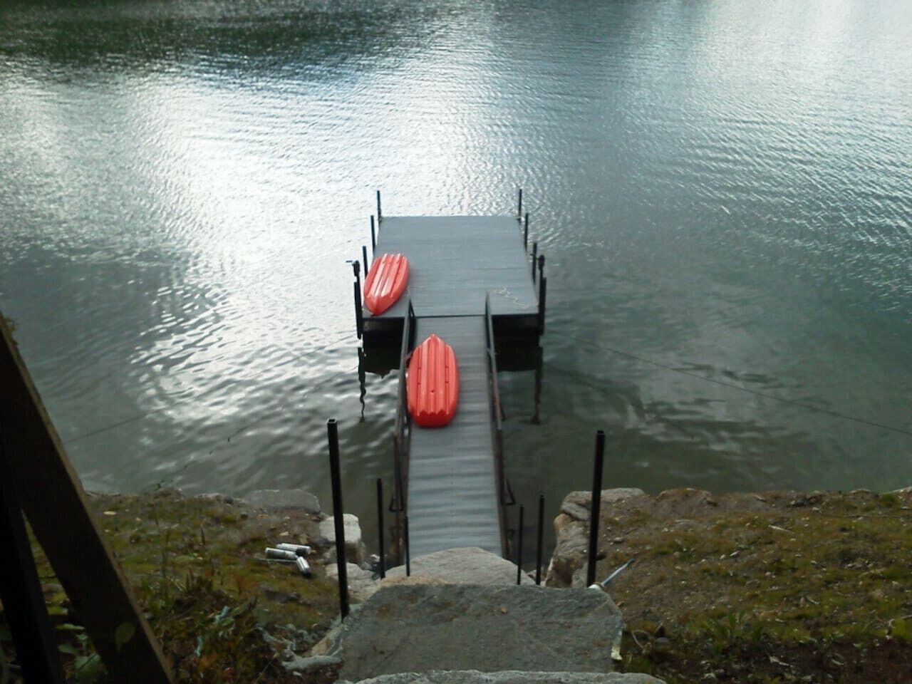 Un muelle de madera que se adentra en una masa de agua tranquila, con dos kayaks rojos.