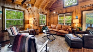 Interior acogedor de una cabaña con paredes de madera, ventanas amplias, un sofá de cuero y una chimenea.