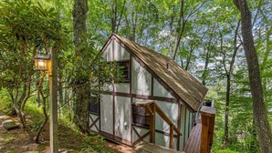 A rustic cabin with a thatched roof, wooden deck, and a lantern post.
