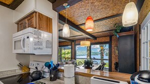 A kitchen with a microwave, kettle, and coffee maker, a dining area with a view of the outdoors, and a rustic ceiling.