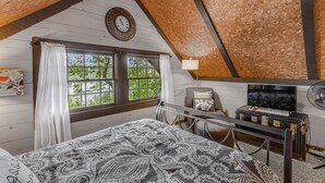 A cozy attic bedroom with a large bed, a clock, and a TV.