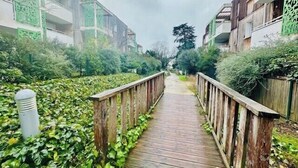 A wooden pathway flanked by greenery and buildings with green lattice windows. - Beautiful apartment - near the beach (La Rochelle)